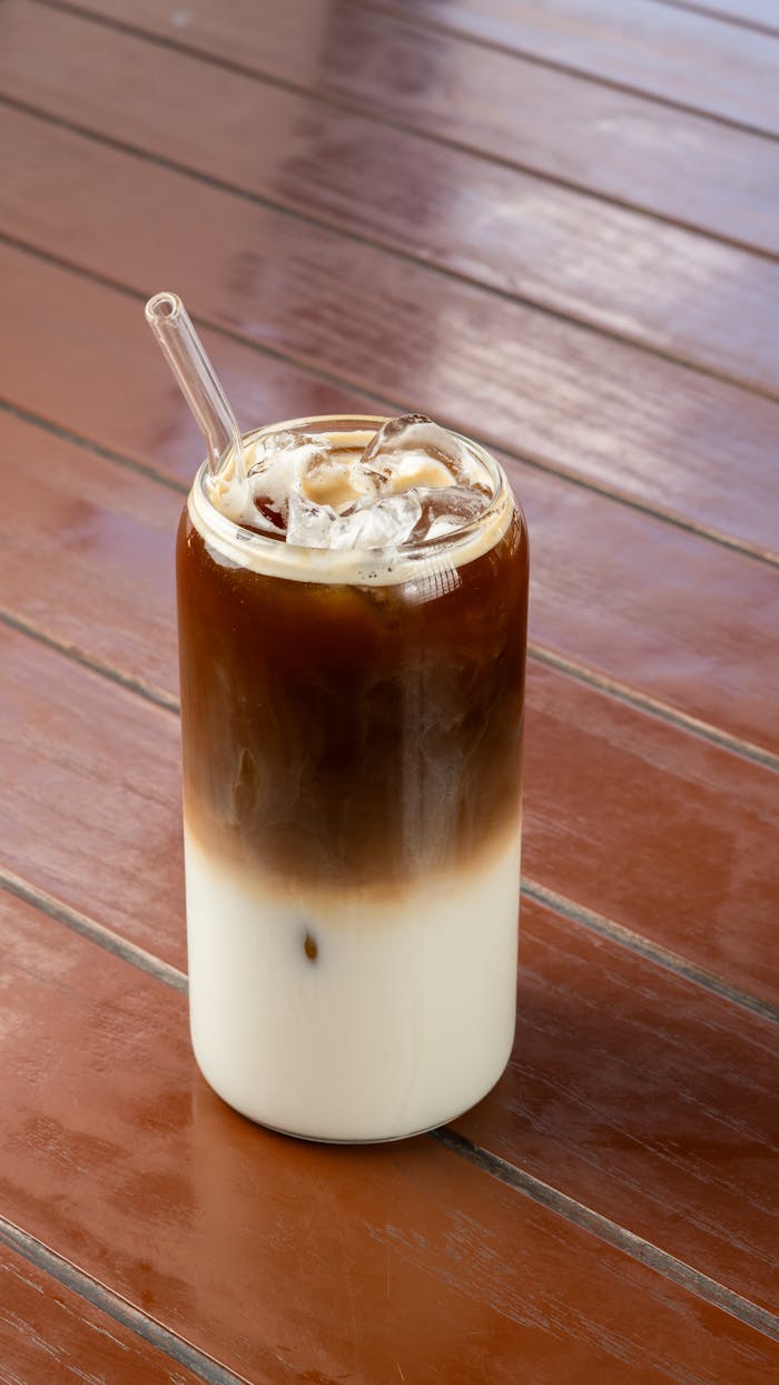about-us Delicious iced coffee served in a glass with straw on a rustic wooden table.