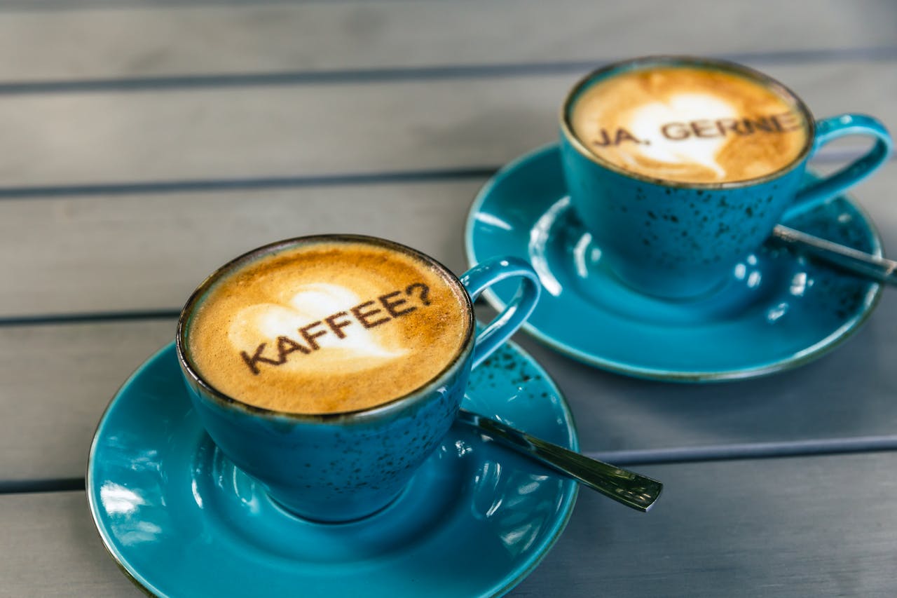 Two cappuccinos with latte art and German text in blue cups on a table.